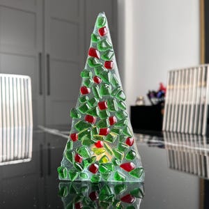 Op de afbeelding: Een decoratieve glazen kerstboom met een driehoekige vorm. De boom is versierd met groene en rode glazen stukjes, die op ornamenten lijken. De boom is ongeveer 15 cm hoog.