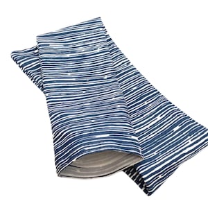 May include: Folded blue and white patterned fabric, possibly a scarf or wrap. The design features horizontal white lines against a dark blue background. The fabric is folded over, revealing a glimpse of the interior lining.