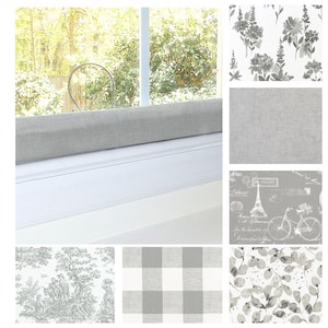 May include: A window with a light gray fabric-covered draft stopper. The image also shows several fabric swatches with various patterns, including floral, linen, toile, buffalo check, and botanical designs, all in shades of gray and white.