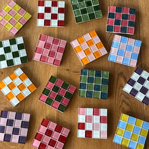 Peut inclure: Une collection de carreaux de mosaïque carrés de différentes couleurs, dont le rose, le vert, l'orange, le bleu et le jaune. Chaque carreau est composé de petits carrés disposés en grille. Les carreaux sont posés sur une surface en bois.