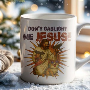 May include: White ceramic mug with the text "DON'T GASLIGHT ME JESUS!" and an illustration of Jesus holding guns with a dog wearing sunglasses. The mug has a curved handle and is set against a snowy background.