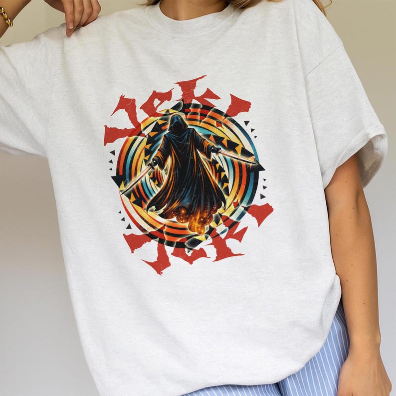 Puede incluir: Camiseta gris claro con un gr&aacute;fico de una figura encapuchada sosteniendo dos espadas, sobre un dise&ntilde;o circular colorido con acentos rojos. El dise&ntilde;o incluye un arco&iacute;ris de colores y formas geom&eacute;tricas.