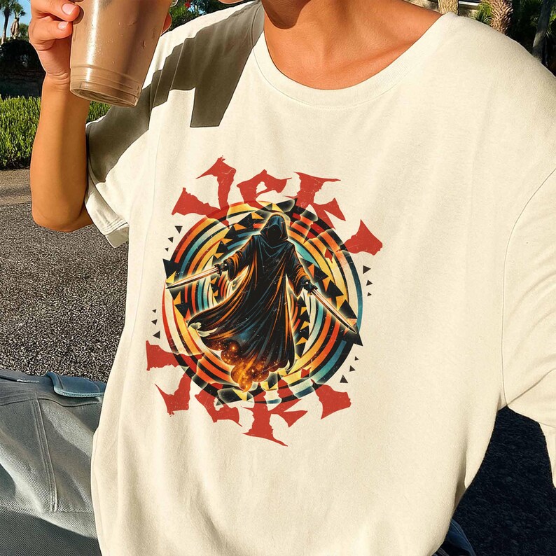 Puede incluir: Camiseta color crema con un gr&aacute;fico de una figura encapuchada sosteniendo dos espadas, sobre un fondo de c&iacute;rculos conc&eacute;ntricos de arco&iacute;ris y detalles rojos. La palabra "Jek" est&aacute; impresa en rojo encima de la figura.