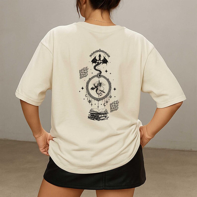 K&ouml;nnte beinhalten: Cremefarbenes T-Shirt mit einem schwarzen Drachendesign auf dem R&uuml;cken. Die Grafik zeigt einen Drachen, einen kreisf&ouml;rmigen Rahmen, Sterne und B&uuml;cher. Das Shirt hat kurze &Auml;rmel und eine lockere Passform.