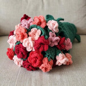 Puede incluir: Un ramo de flores de ganchillo hecho a mano con una variedad de flores coloridas. El ramo incluye flores rojas, rosas y color coral con hojas y tallos verdes. Las flores están dispuestas en un haz, creando una exhibición visualmente atractiva y texturizada.