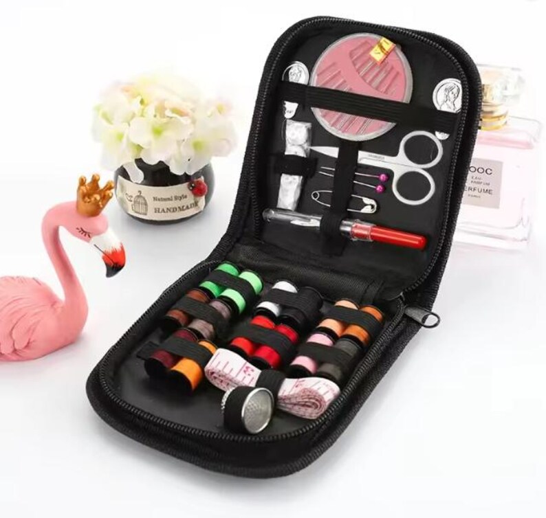 Peut inclure: Trousse de couture noire zipp&eacute;e, ouverte pour r&eacute;v&eacute;ler diverses fournitures de couture. Comprend des bobines de fil de diff&eacute;rentes couleurs, des aiguilles, des ciseaux, un m&egrave;tre ruban et d'autres outils. Un kit compact et organis&eacute;.