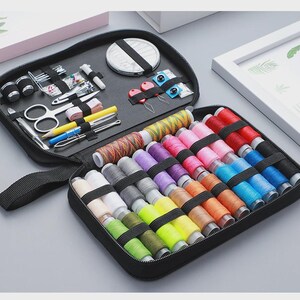 Peut inclure: Trousse de couture noire zipp&eacute;e contenant divers outils de couture et une vari&eacute;t&eacute; de bobines de fil color&eacute;es. Le kit comprend des ciseaux, des aiguilles, un m&egrave;tre ruban et d'autres fournitures de couture essentielles. Les bobines de fil sont de diff&eacute;rentes couleurs.
