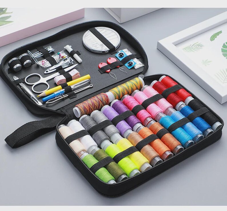 Peut inclure: Trousse de couture noire zipp&eacute;e contenant divers outils de couture et une vari&eacute;t&eacute; de bobines de fil color&eacute;es. Le kit comprend des ciseaux, des aiguilles, un m&egrave;tre ruban et d'autres fournitures de couture essentielles. Les bobines de fil sont de diff&eacute;rentes couleurs.