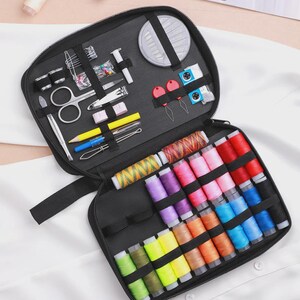 Peut inclure: Trousse de couture noire ouverte, r&eacute;v&eacute;lant divers outils de couture et des bobines de fil color&eacute;es. Le kit comprend des ciseaux, des aiguilles, du fil et d'autres fournitures essentielles pour les projets de couture. Le mot "Feeling" est visible en arri&egrave;re-plan.