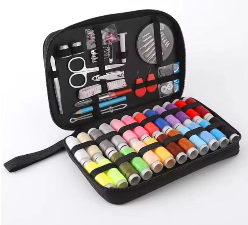 Peut inclure: Trousse de couture noire zipp&eacute;e, ouverte pour r&eacute;v&eacute;ler divers outils de couture et une s&eacute;lection de bobines de fil color&eacute;es. Comprend des ciseaux, des aiguilles, des d&eacute;s &agrave; coudre et un m&egrave;tre ruban.