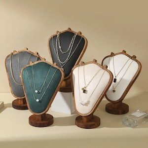 May include: Five wooden jewelry display stands with various necklaces. The stands have different colored fabric backgrounds: gray, teal, black, and white. The necklaces are gold and silver, with pearls and gemstones.