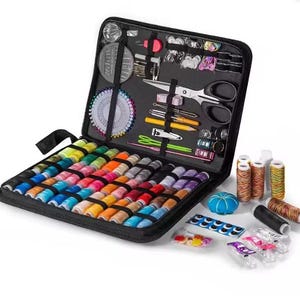 Peut inclure: Trousse de couture noire ouverte, contenant une vari&eacute;t&eacute; de bobines de fil color&eacute;es, des ciseaux, des aiguilles, des &eacute;pingles et d'autres accessoires de couture. Le kit comprend un coussin &agrave; &eacute;pingles, des boutons et du fil.