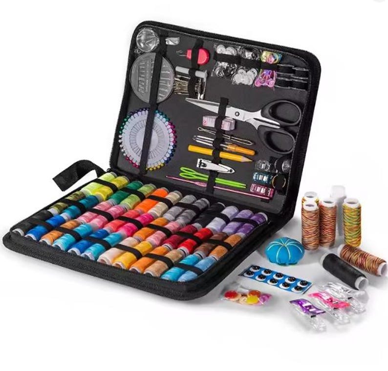 Peut inclure: Trousse de couture noire ouverte, contenant une vari&eacute;t&eacute; de bobines de fil color&eacute;es, des ciseaux, des aiguilles, des &eacute;pingles et d'autres accessoires de couture. Le kit comprend un coussin &agrave; &eacute;pingles, des boutons et du fil.
