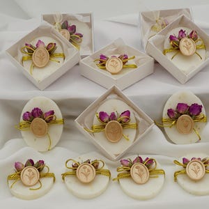 May include: Oval and round soaps with floral and gold accents. Each soap is decorated with dried purple flowers and a wooden emblem. Some soaps are packaged in white boxes, creating a luxurious presentation.