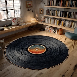 May include: A round black rug designed to resemble a vintage vinyl record. The rug features concentric grooves and a central label with orange, blue, and white tones. The rug is placed on a light-colored wooden floor, creating a retro aesthetic.
