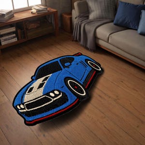 May include: A blue car-shaped rug with black and white accents. The rug features a detailed design of a sports car, with red trim and white wheels. The rug is placed on a wooden floor.