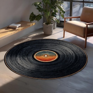 May include: A round black rug designed to resemble a vintage vinyl record. The rug features concentric grooves and a central label with orange, blue, and white tones. The rug is placed on a light-colored wooden floor.