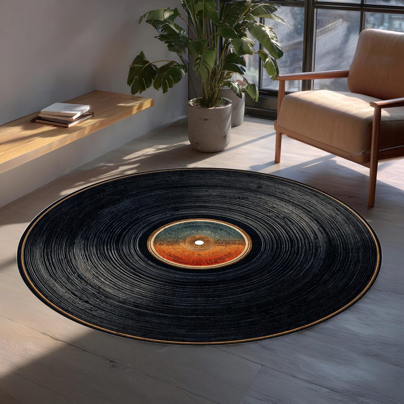May include: A round black rug designed to resemble a vintage vinyl record. The rug features concentric grooves and a central label with orange, blue, and white tones. The rug is placed on a light-colored wooden floor.