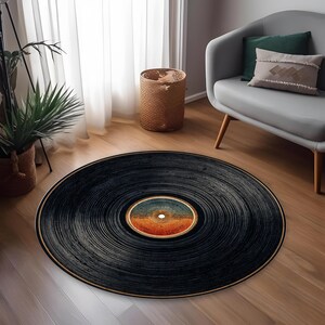 May include: A round black rug designed to resemble a vinyl record. The rug features concentric grooves and a central label with orange, blue, and white hues. The rug is placed on a wooden floor.