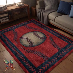 Op de afbeelding: Een rechthoekig rood tapijt met een honkbalontwerp. Het tapijt heeft een grote honkbal in het midden, omgeven door een donkerblauwe rand en honkbalstikseldetails. Het tapijt ligt op een houten vloer.