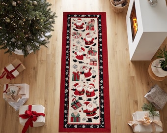 Op de afbeelding: Een rechthoekige kerstlopermat met een rode rand en een crèmekleurig middenstuk. Het heeft figuren van de kerstman, sneeuwvlokken en geschenkdozen. De loper ligt op een houten vloer, met een kerstboom en ingepakte cadeaus in de buurt.