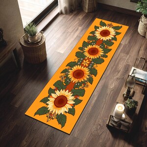 Puede incluir: Una alfombra de pasillo naranja con un patrón repetido de girasoles. Los girasoles tienen centros marrones y pétalos amarillos, con hojas verdes y pequeñas flores amarillas. La alfombra es rectangular y está colocada sobre un suelo de madera oscura.