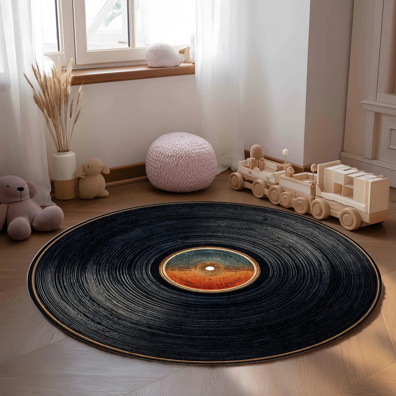 May include: A round rug designed to resemble a vinyl record. The rug is primarily black with concentric grooves and a colorful label in the center. The rug is placed on a wooden floor, with other decorative items in the background.
