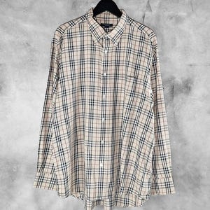 May include: A beige plaid long-sleeved shirt with black, red, and white lines. The shirt features a button-down collar and a chest pocket. It is hanging on a black hanger. The shirt is made of a lightweight fabric, suitable for various occasions.