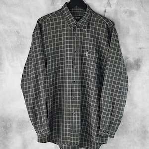 May include: A long-sleeved shirt with a green and white check pattern, suspended from a black hanger. The shirt features a button-down collar, a chest pocket, and a small logo. The fabric appears lightweight and suitable for various occasions.