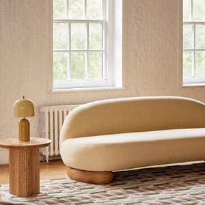 Peut inclure: Int&eacute;rieur de salon moderne avec un canap&eacute; cr&egrave;me aux formes arrondies, une table d'appoint en bois avec une lampe et un tapis &agrave; motifs. Le tapis pr&eacute;sente un bord ondul&eacute; et un motif g&eacute;om&eacute;trique dans les tons de vert, marron et cr&egrave;me.