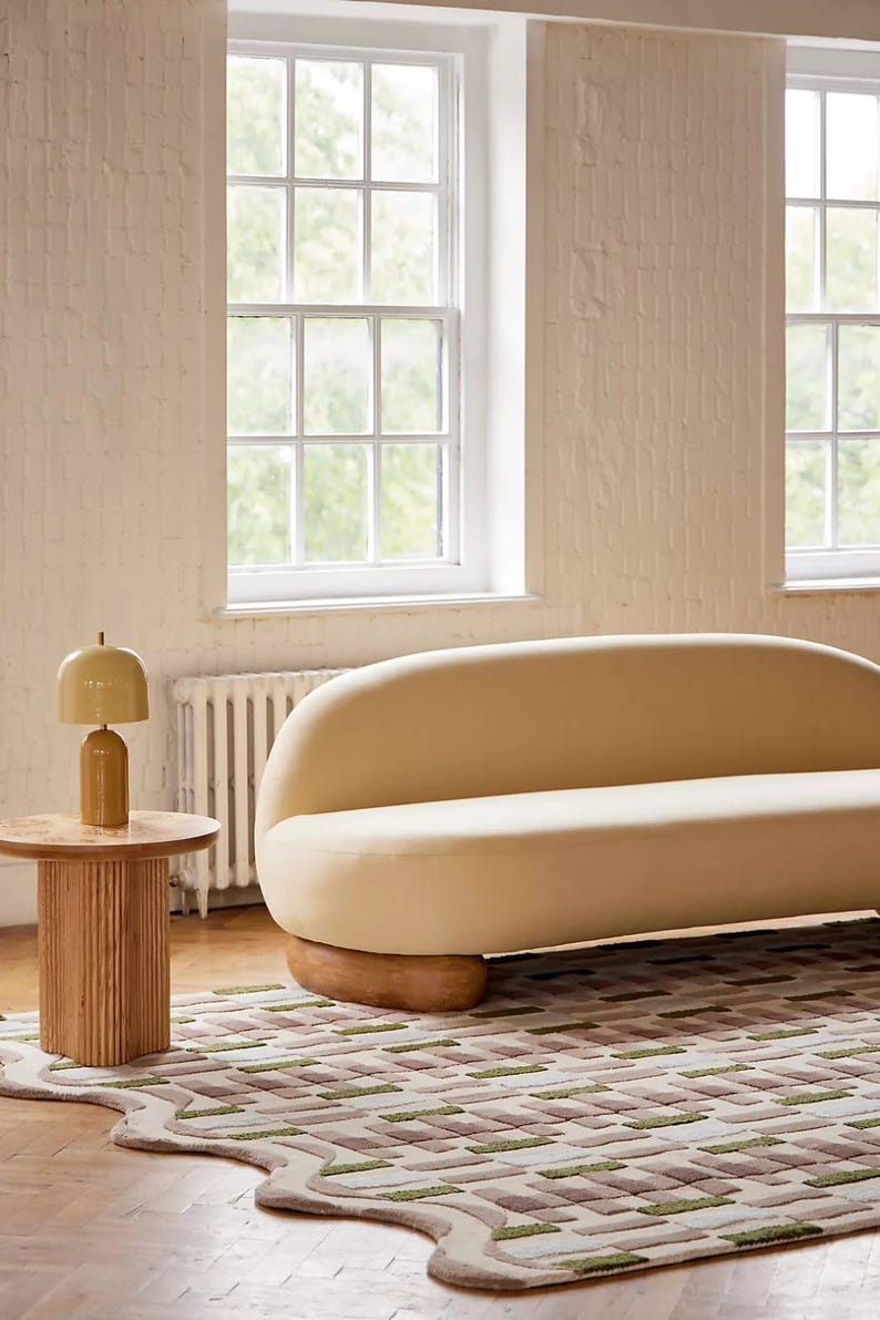 Peut inclure: Int&eacute;rieur de salon moderne avec un canap&eacute; cr&egrave;me aux formes arrondies, une table d'appoint en bois avec une lampe et un tapis &agrave; motifs. Le tapis pr&eacute;sente un bord ondul&eacute; et un motif g&eacute;om&eacute;trique dans les tons de vert, marron et cr&egrave;me.