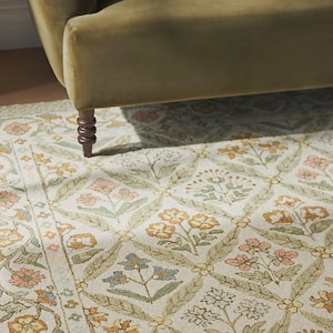 May include: A floral patterned area rug with a cream background and a repeating design of flowers in shades of pink, yellow, and blue. The rug is partially under a green sofa.