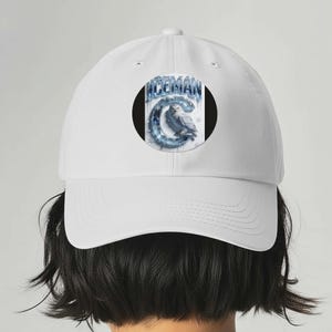 Op de afbeelding: Witte baseballcap met een cirkelvormig ontwerp met het woord "ICEMAN" in blauw en een illustratie van een sneeuwuil. Het ontwerp is geplaatst tegen een zwarte achtergrond. De cap heeft een klassiek zes-panelen ontwerp.