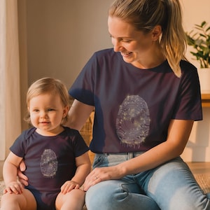 May include: A dark navy blue short-sleeved t-shirt and a matching infant bodysuit, both featuring a central graphic of a white fingerprint design with small yellow star-like accents scattered throughout the pattern on the front of each garment.