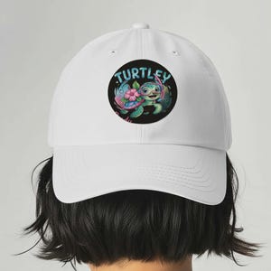 Può includere: Cappellino da baseball bianco con una grafica circolare con la scritta "TURTLEY" sopra una tartaruga dei cartoni animati con occhiali e un fiore. La tartaruga è verde, blu e rosa. Il cappellino ha una visiera curva e una corona strutturata.