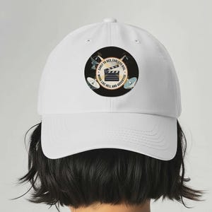 May include: White baseball cap with a circular graphic featuring a film clapperboard and the text "Early to bed, early to rise, work like hell and advertise."
