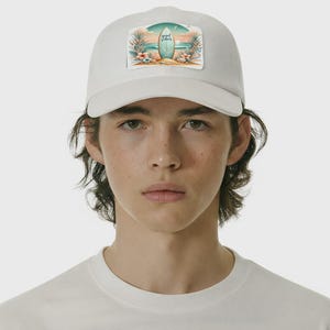 Puede incluir: Gorra de béisbol blanca con un parche rectangular que muestra una tabla de surf y una escena de playa, con la inscripción "good vibes". La gorra tiene una visera curva.