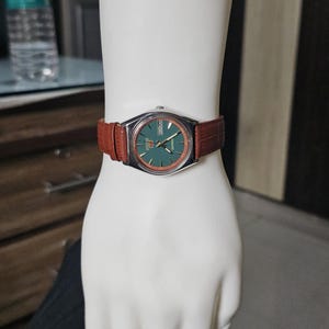 May include: A vintage Seiko watch with a green dial and silver case, displayed on a mannequin hand. The watch has a brown leather band. The text "etsy shop- vintageautowind" is visible.