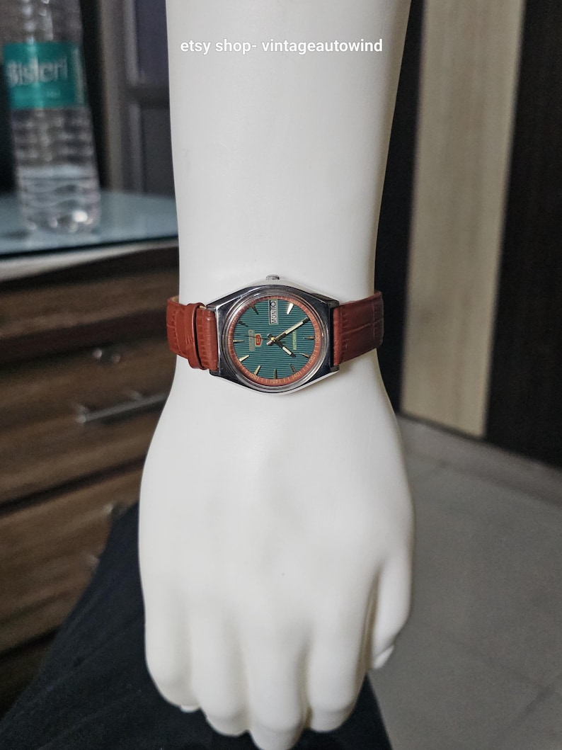 May include: A vintage Seiko watch with a green dial and silver case, displayed on a mannequin hand. The watch has a brown leather band. The text "etsy shop- vintageautowind" is visible.