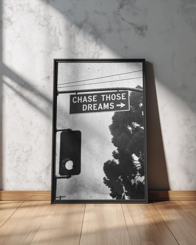 Może przedstawiać: Czarno-biała oprawiona grafika z napisem "CHASE THOSE DREAMS" ze strzałką. Obraz zawiera sygnalizację świetlną i drzewo na tle pochmurnego nieba. Rama jest czarna, a grafika jest wyświetlana na drewnianej podłodze.