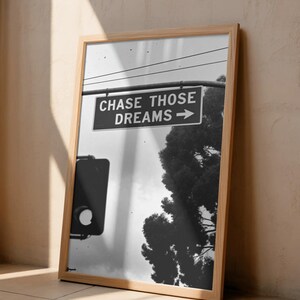 Może przedstawiać: Czarno-biała oprawiona grafika z napisem "CHASE THOSE DREAMS" ze strzałką. Obraz zawiera sygnalizację świetlną i drzewo. Rama wykonana jest z jasnego drewna.