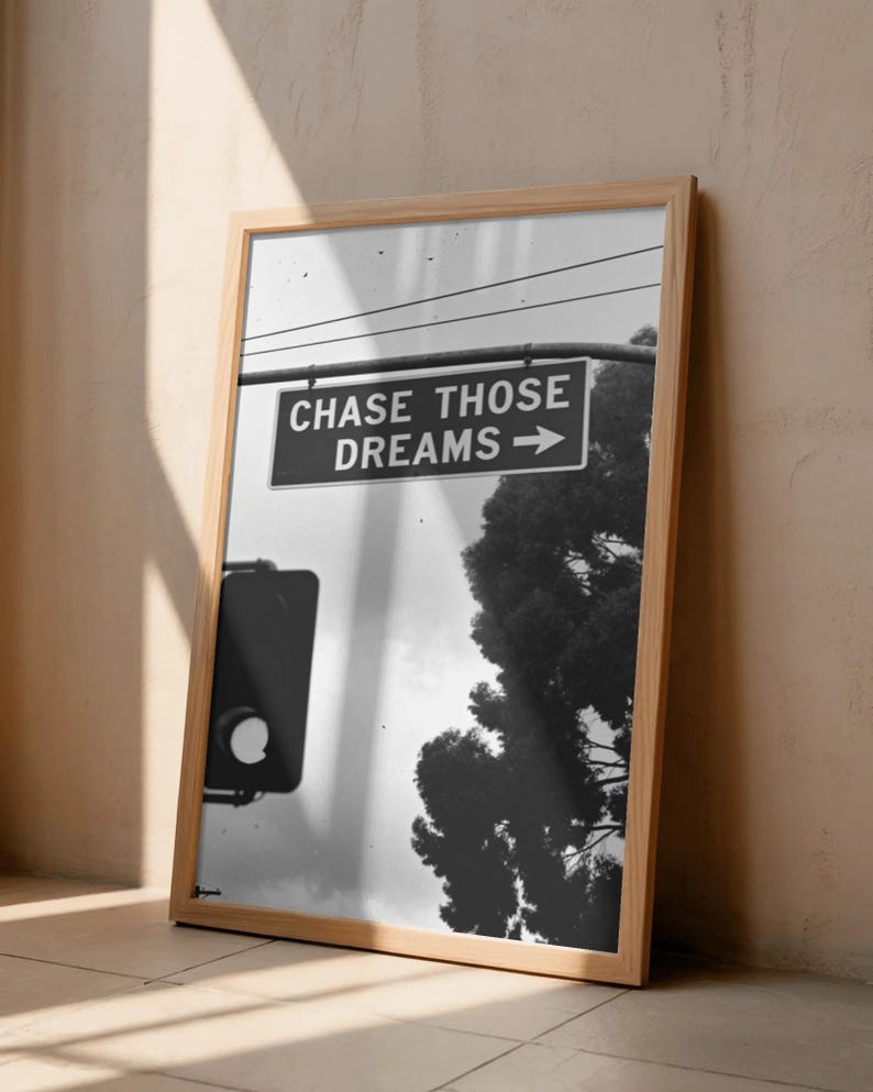 Może przedstawiać: Czarno-biała oprawiona grafika z napisem "CHASE THOSE DREAMS" ze strzałką. Obraz zawiera sygnalizację świetlną i drzewo. Rama wykonana jest z jasnego drewna.