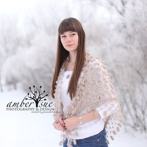 May include: A beige crocheted shawl with a floral pattern and tassel trim. The shawl is draped over a white sweater and blue jeans. The image includes the text "amber sue PHOTOGRAPHY & DESIGN rooted & grounded in love."