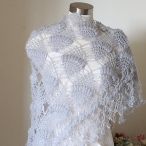 May include: A delicate gray crocheted shawl with a lacy pattern and fringe. The shawl is draped over a white mannequin.