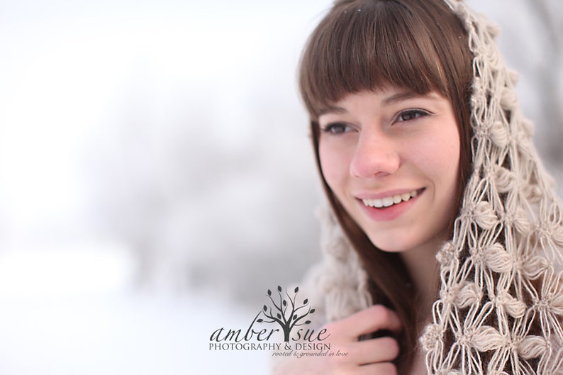 May include: A woman with brown hair and a beige crocheted hood smiles in a snowy outdoor setting. The hood features a floral pattern. The image includes the text "amber sue photography & design rooted & grounded in love."