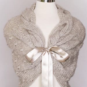 May include: A beige knitted shawl with a satin ribbon tied in a bow at the neck.