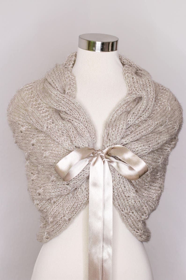 May include: A beige knitted shawl with a satin ribbon tied in a bow at the neck.