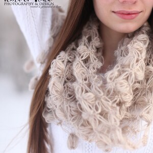 May include: A close-up of a beige infinity scarf with a textured, looped design. The scarf is worn over a white sweater. The image also shows long brown hair and the logo "amber sue photography & design".