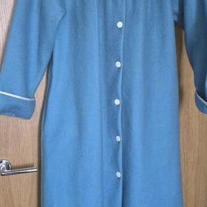 May include: A teal dressing gown with white trim and button fastenings. The gown has white leaf embroidery on the collar. The sleeves have white trim at the cuffs. A comfortable garment for relaxing.