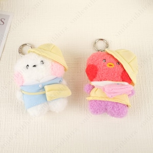 May include: Two plush keychains: one white with pink accents and a blue outfit, the other red with purple accents and a yellow outfit. Both have yellow hats and silver key rings. The keychains are designed to resemble cartoon characters.